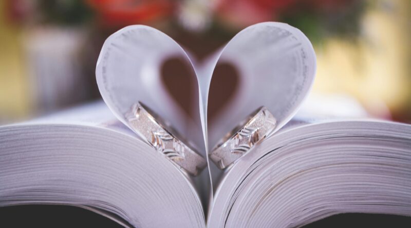 Close-up of wedding rings on heart-shaped book pages symbolizing love and romance.