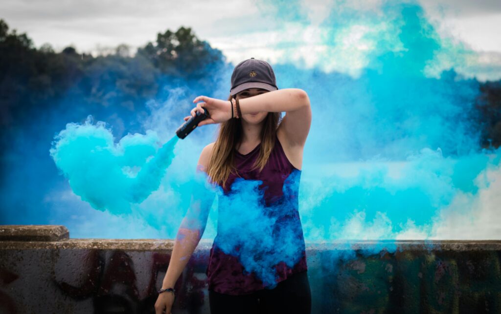 pexels-photo-445109-445109 A stylish woman surrounded by bright blue smoke outdoors, creating a dynamic fashion statement.