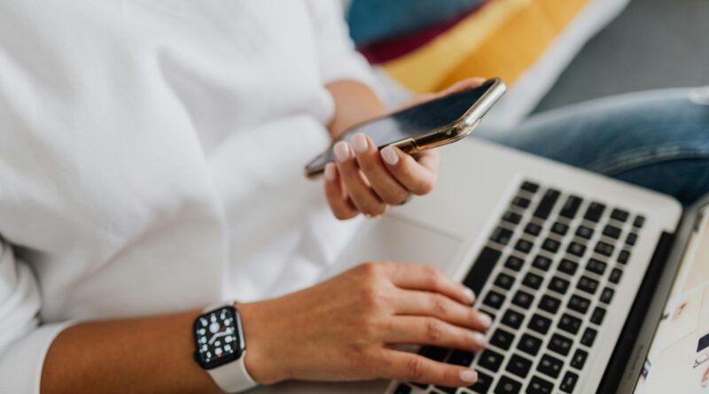 Close-up of a person using a smartphone and laptop for work, showcasing multitasking in a modern home office setting.